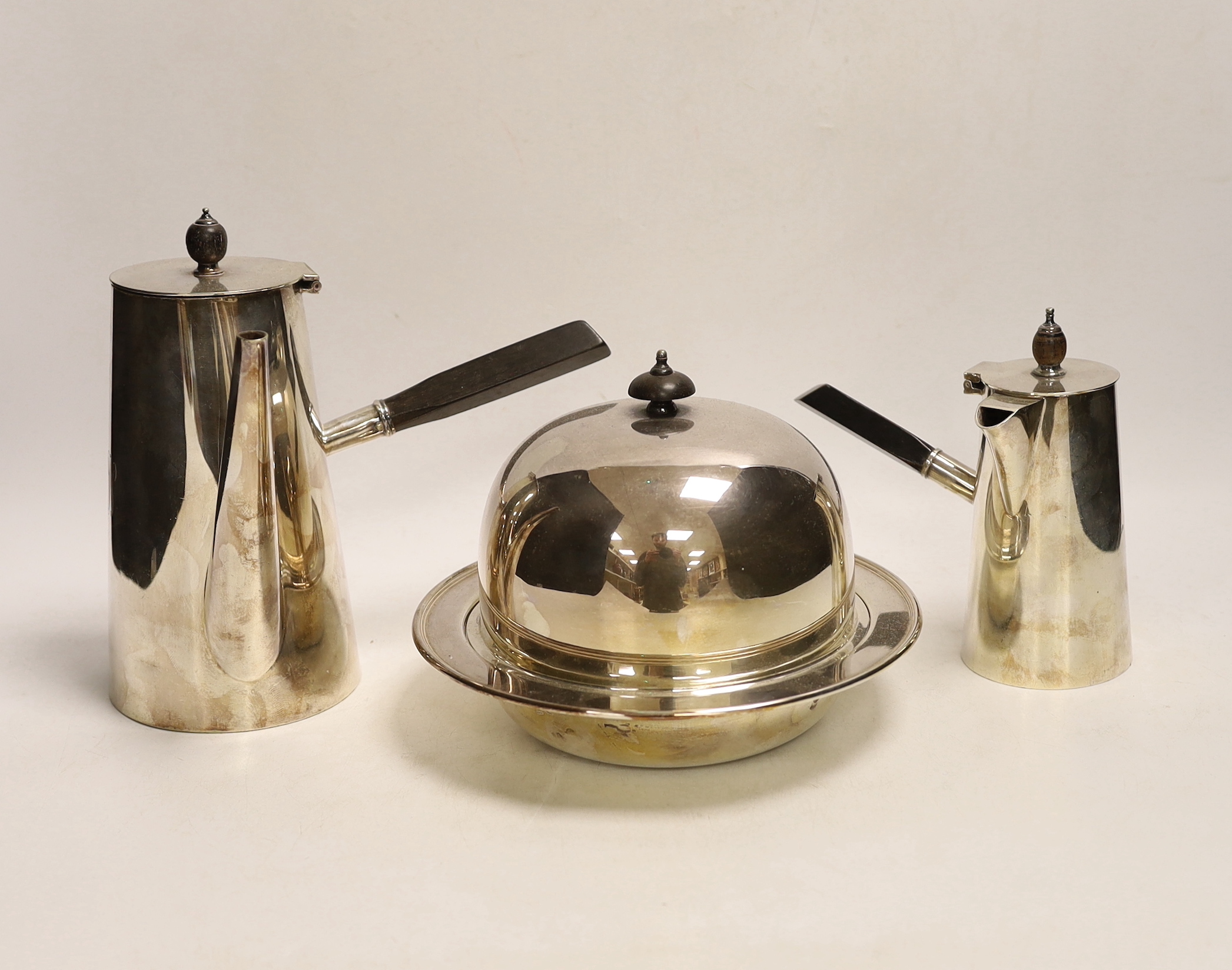 Two silver plated cafe au lait pots, one with double walled interior and a muffin dish, each with ebonised handles, largest 20cm high